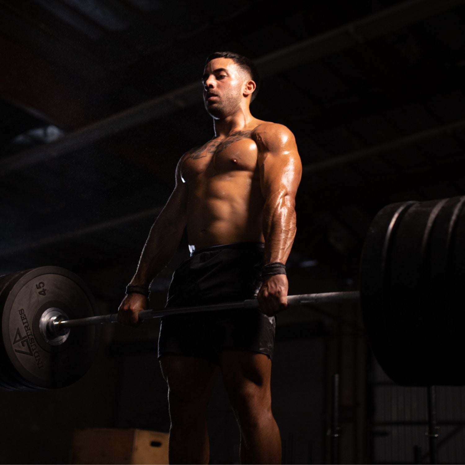 Fit athlete deadlifting a heavy barbell in a dark gym