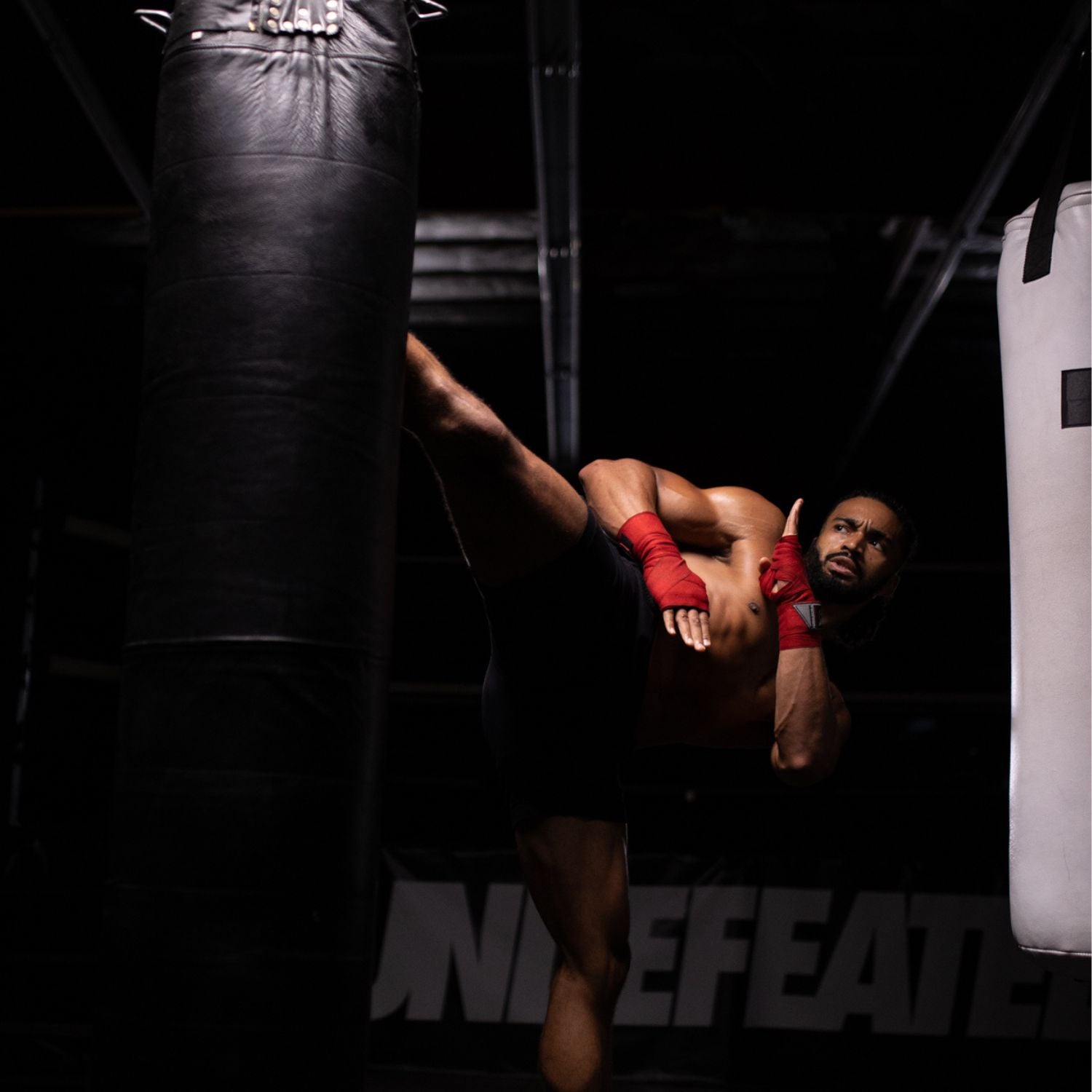 Very fit kickboxer high-kicking a heavy bag in a dark gym 